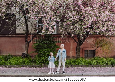Family (mother and children) in spring city street with pink japanese cherry trees blossom (Uzhhorod City, Ukraine). Sakura blossomed. Young mother with her child have fun in the park near the sakura.