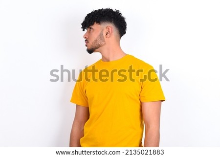 Close up side profile photo young arab man wearing yellow T-shirt over white background not smiling attentive listen concentrated