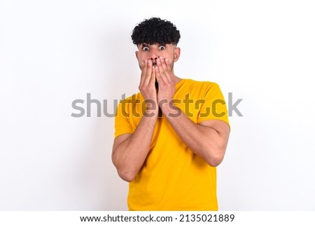 Vivacious young arab man wearing yellow T-shirt over white background , giggles joyfully, covers mouth, has natural laughter, hears positive story or funny anecdote