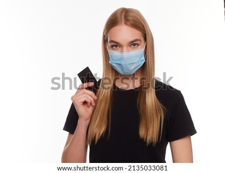 woman with credit card wearing a medical mask isolated on a white background. Conceptual photo, purchases with cashless payment during quarantine.