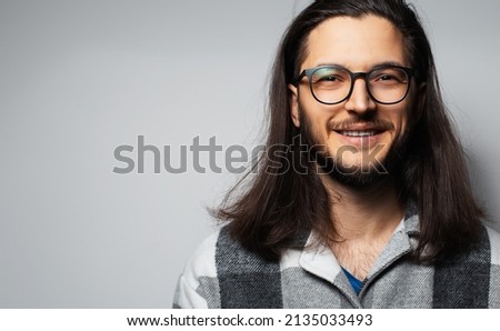 Studio portrait of handsome smiling man with long hair on  grey background.