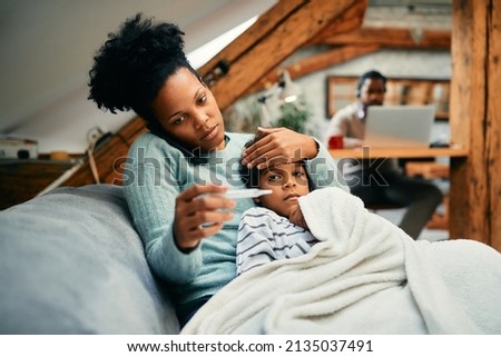 African American mother measuring sick son's temperature while talking to the doctor over the phone. Royalty-Free Stock Photo #2135037491