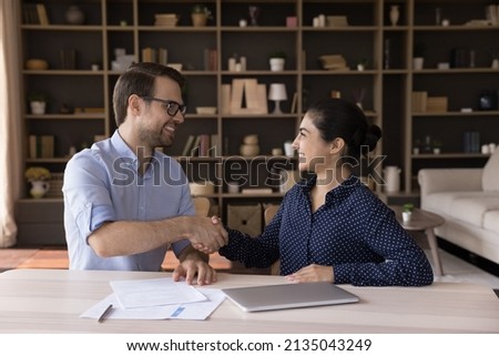 Smiling millennial businessman shake hand of happy Indian female colleague partner consultant grateful for advice appreciate for collaboration. Two business people handshake reach agreement make deal Royalty-Free Stock Photo #2135043249