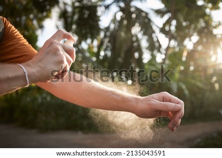 Prevention against mosquito bite in tropical destination. Man applying insect repellent on his hand against palm trees. Royalty-Free Stock Photo #2135043591