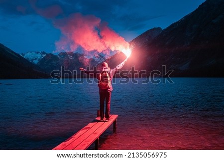 The hiker on the pier lit the emergency red torch and calling for help. Rescue flare and sos signal concept Royalty-Free Stock Photo #2135056975