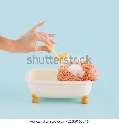 Hand of young woman washing human brain with brush in bath tub with foam on pastel blue coloured background. Minimal abstract concept of psychology, head, Mental health, brain fog or brainwashing. Royalty-Free Stock Photo #2135060245