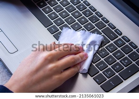 Woman cleaning laptop keyboard with a white cloth.