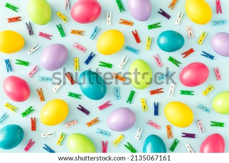 Colorful pattern made of Easter eggs and laundry clips on pastel blue background. Creative holiday wallpaper concept. Minimal top view flat lay composition.