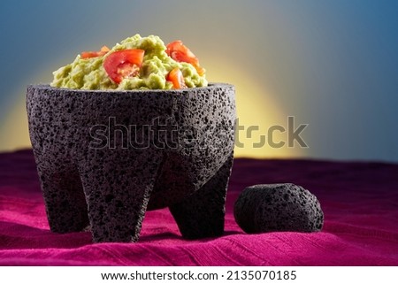 Delicious guacamole with avocado and cherry tomatoes in a typical Mexican mortar or molcajete over a purple tablecloth and a sunrise on the background Royalty-Free Stock Photo #2135070185
