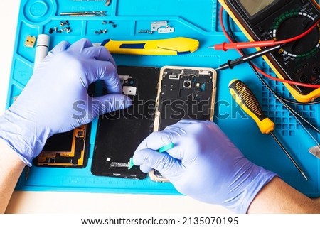 Craftsman in rubber gloves repair or service a mobile phone on a special rubber mat for repair. view from the inside. Fixing the gadget. Broken smartphone