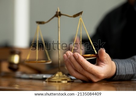A lawyer is trying his hand under the scales of justice, he is a lawyer who has to uphold the principles of fairness and justice. Lawyer concept and the use of law properly and fairly. Royalty-Free Stock Photo #2135084409
