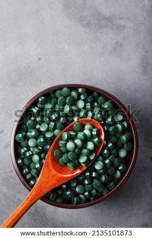 Organic spirulina tablets in a wooden cup with a wooden spoon on a dark background with free space top view