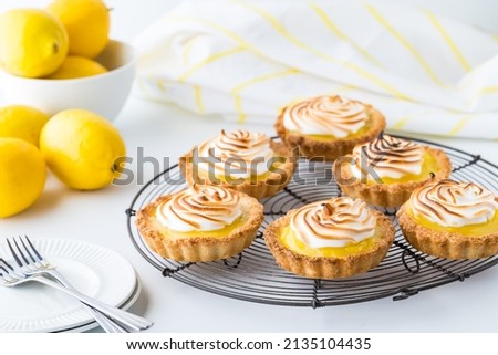 A cooling rack with homemade lemon meringue tartlets and lemons in behind.