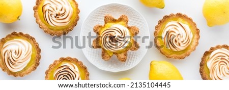 A narrow view of lemons and lemon meringue tartlets with one on a serving plate.
