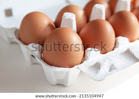 Cardboard egg box with brown eggs on white background.