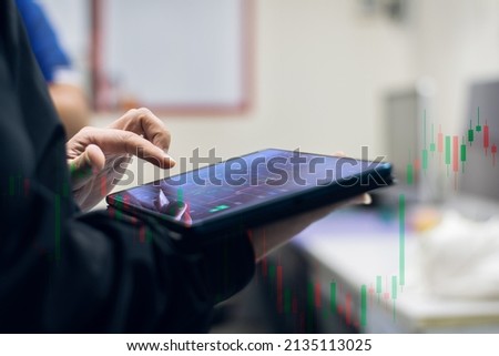 A young man in a robe operates a digital schematic screen of a mobile tablet with his hands. And use your hand to scroll the screen and see the stock chart that is currently displayed.