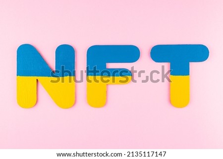 NFT (Non-Fungible Token) in Ukrainian flag colors. Blue-yellow NFT inscription on pink background. Ukraine support concept. Top view. Copy space