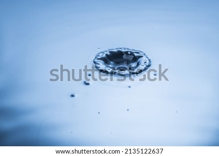 Close up view of falling drops on blue water surface isolated on background.