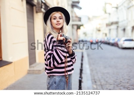 Charming hipster girl in hat with retro camera in city. Travel concept, lifestyle