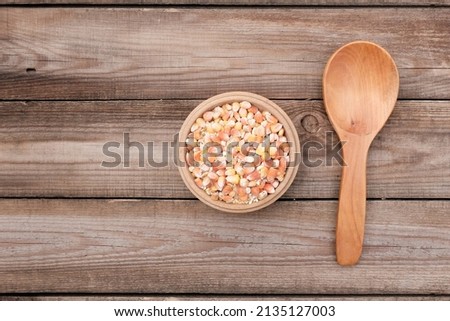Dried corn seeds in a wooden plate, bowl, next to an empty spoon on a light wood background. The concept of harvest, price increase, export, import