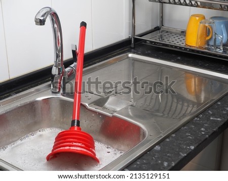 Clogged pipes in the kitchen. Sink full of dirty water, red plunger Royalty-Free Stock Photo #2135129151