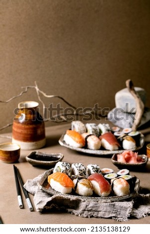 Sushi rolls set for two. Traditional japanese dish sushi and rolls with fresh salmon, tuna, eel and prawns on rice. Serving on plates with soy sauce and sake on brown table. Japanese style dinner