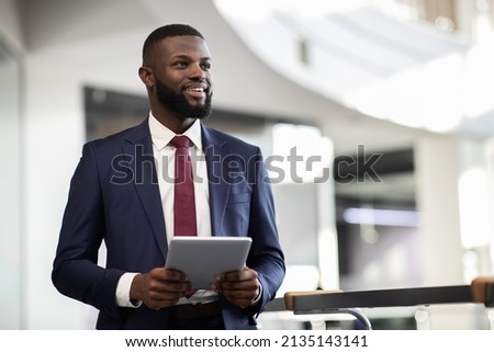 Cheerful young bearded african american man manager walking by office building corridor, holding modern digital tablet, using mobile app for business, looking at copy space and smiling, panorama Royalty-Free Stock Photo #2135143141