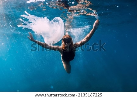 Woman underwater with jellyfish in blue ocean. Lady glides underwater in transparent sea Royalty-Free Stock Photo #2135167225