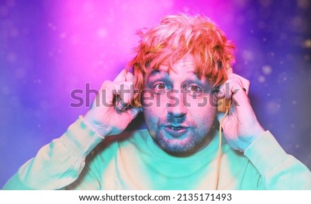 Happy hipster man listening to music with headphones at black studio with neon lights. Disco, night club, hip hop style, positive emotions, face expression, dancing concept.