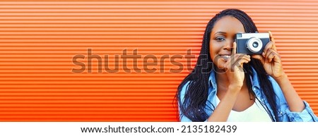 Portrait of happy smiling african woman photographer with film camera on red background, blank copy space for advertising text