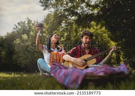 couple of twenties young people on vacation playing music and singing loud outdoor drinking wine at picnic - millennials carefree have fun together on the summer weekend outing  Royalty-Free Stock Photo #2135189773