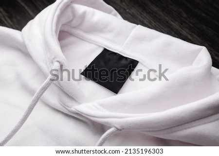 Blank clothing label on the texture of a white sweater hoodie. Label with empty space for text