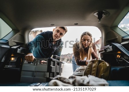 Two people couple students travel concept man and woman taking luggage baggage suitcase and other stuff and belongings from the back of car while moving into dormitory on college campus real people Royalty-Free Stock Photo #2135197029