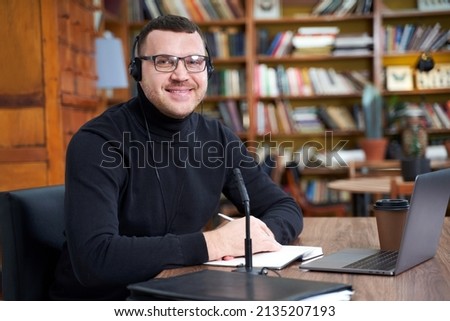 Male blogger streaming from library using laptop and microphone