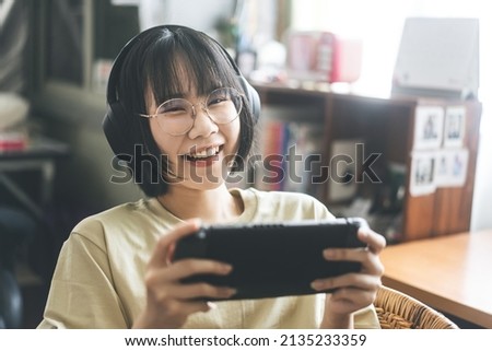 Nerd style young adult asian gamer woman wear eyeglasses and headphone play a online game. Competition for victory mood. Happy people leisure lifestyle at home.