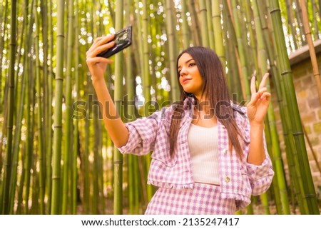 Young caucasian girl with a pink skirt in a bamboo forest. Enjoying summer holidays in a tropical climate, a girl lifestyle doing a selfie in the forest