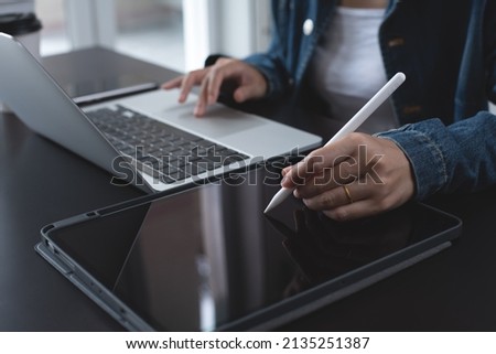 Close up of business woman in casual wear using stylus pen touching on digital tablet screen on office desk at home. Female entrepreneur, freelancer working on tablet pc with smart phone on table