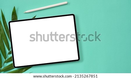 Top view, Tablet touchpad empty screen mockup with stylus pen and palm leave on green background.