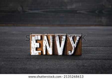 ENVY. Text from alphabet blocks on a dark wooden background.