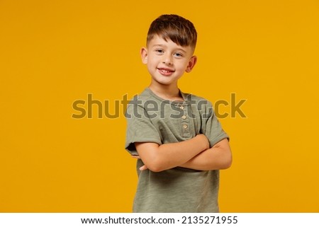 Little small fun smiling happy boy 6-7 years old wearing green casual t-shirt hold hands crossed folded isolated on plain yellow background studio portrait. Mother's Day love family lifestyle concept Royalty-Free Stock Photo #2135271955