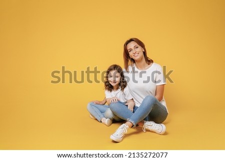 Full body length happy woman in basic white t-shirt have fun sit on floor with child baby girl 5-6 years old Mom little kid daughter isolated on yellow color background studio Mother's Day love family