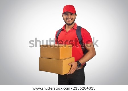 Portrait Of Young Delivery Man Holding Cardboard Box Against Grey Background Royalty-Free Stock Photo #2135284813