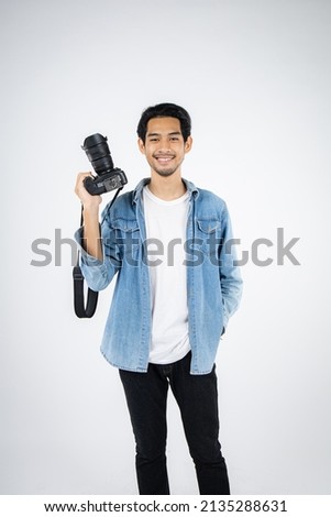 Handsome young photographer poses with smiles and holding professional digital camera in the studio.