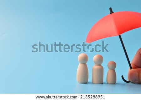 Red toy umbrella and wooden doll figures isolated on a blue background. Insurance coverage concept. Royalty-Free Stock Photo #2135288951