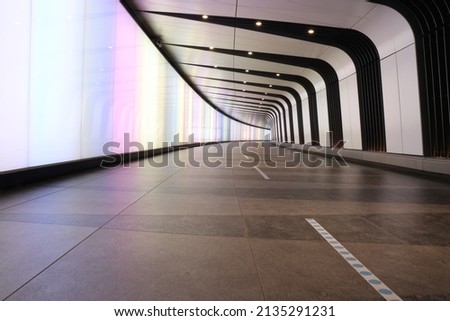 A city urban image taken from a low angle looking along a tunnel curving to the right.  Coloured light fill the left wall while the right is alternate black and white bands.