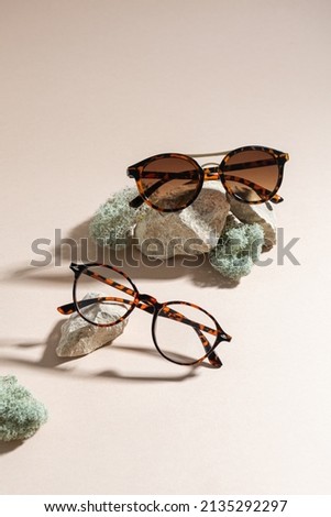 Trendy sunglasses and eyeglasses on a beige background. Close up. Sunglasses and spectacles sale concept. Optic shop promotion banner. Eyewear fashion. Minimalism. Vertical Royalty-Free Stock Photo #2135292297