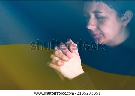 Sad woman with Ukraine flag at background praying. Concept of standing with Ukrainian nation in war with Russia.