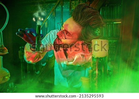 Chemistry professor enthusiastically conducts chemical experiments in his laboratory filled with mysterious green and red light and haze. Vintage style. Royalty-Free Stock Photo #2135295593