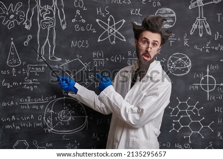 A funny smart scientist stands at the blackboard trying to explain scientific formulas and diagrams. Science and education. Royalty-Free Stock Photo #2135295657
