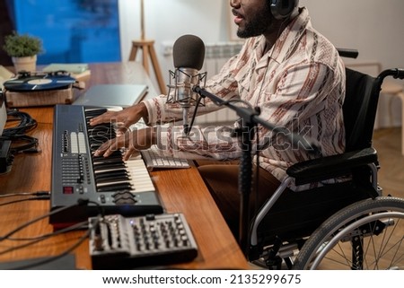 Mid section of African American performer with disability playing piano keyboard and singing while recording his music and songs Royalty-Free Stock Photo #2135299675